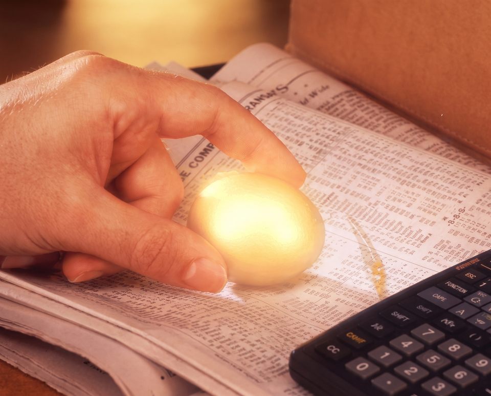 A hand holding a glowing golden egg over financial pages, beside a calculator